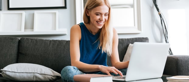happy-woman-sitting-on-sofa-and-using-laptop-at-home